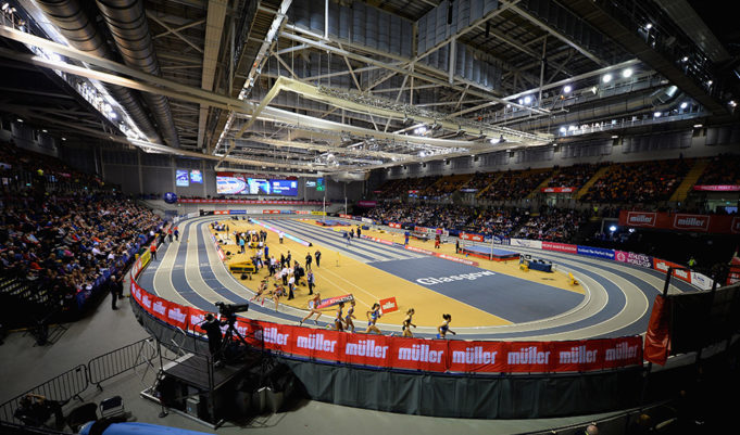A panoramic shot of the indoor track at Glasgow with femal athletes sprinting around it