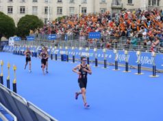 Triathletes racing on blue matting in front of a crowd of spectators sitting in stands