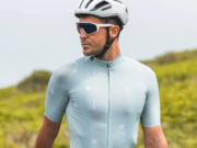 Male cyclist wearing pale blue cycling jersey stands next to bike