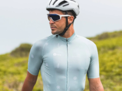 Male cyclist wearing pale blue cycling jersey stands next to bike