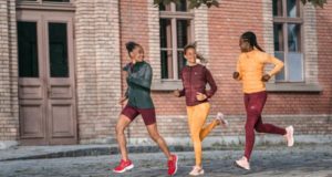Three female runners run past a brick building, they are all smiling
