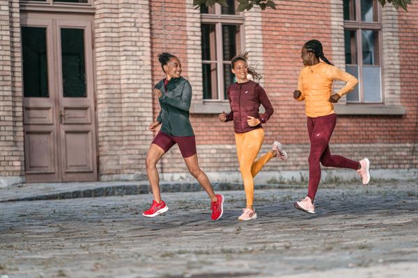 Three female runners run past a brick building, they are all smiling