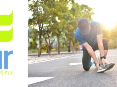 A runner in the road kneeling down holding their ankle. Sunshine in the backgground.