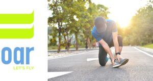 A runner in the road kneeling down holding their ankle. Sunshine in the backgground.