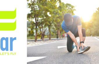 A runner in the road kneeling down holding their ankle. Sunshine in the backgground.