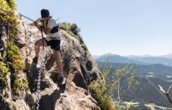 Photo of a runner scaling a high up rock face, with the aid of an iron chain.