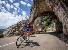 A cyclist exits a tunnel carved out of rock on the side of a mountain