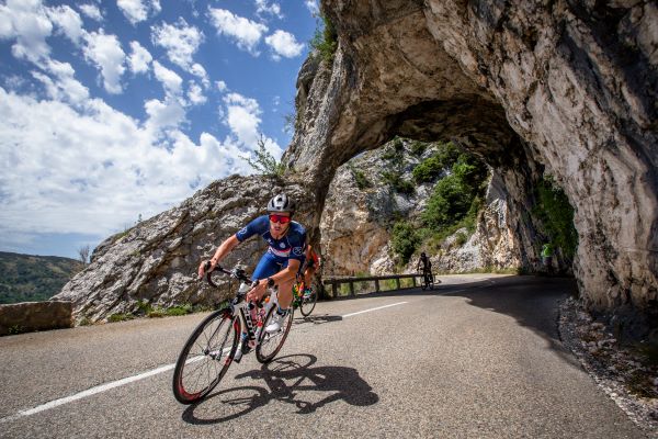 A cyclist exits a tunnel carved out of rock on the side of a mountain