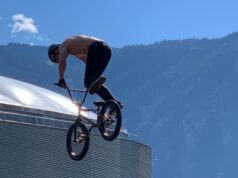 Cyclist on BMX jumps in air, with building benhind, and mountains behind the building.
