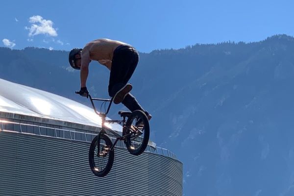 Cyclist on BMX jumps in air, with building benhind, and mountains behind the building.