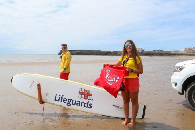 Image of a male and femal lifeguard on a beach with a paddleboard saying 'Lifeguards'