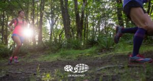 Two trail runners in woods with the sun shining through the trees