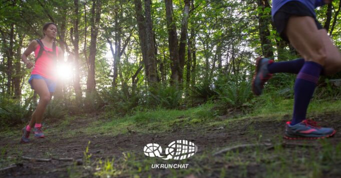 Two trail runners in woods with the sun shining through the trees