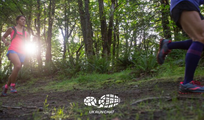 Two trail runners in woods with the sun shining through the trees