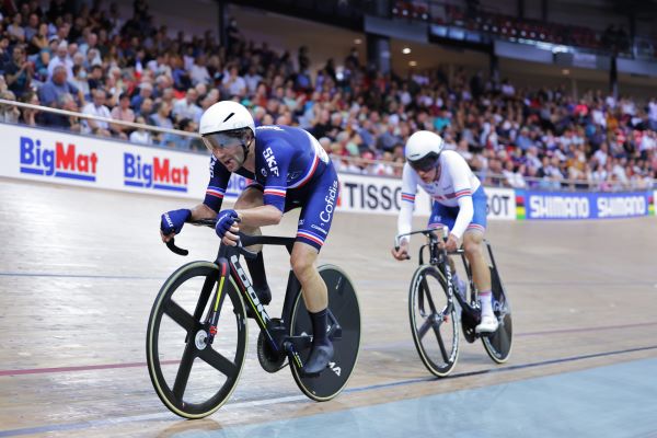 Two cyclists on an indoor track with BigMat printed on the track edging