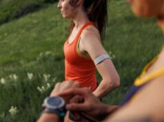 A female runner wearing a red vest wears a white heartrate monitor around her left arm.