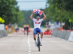 Fin Graham cycles while holding the union flag above his head with a look of pure joy on his face.