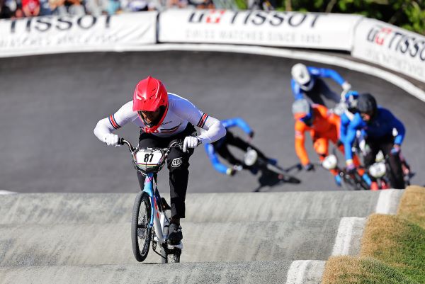 Kye Whyte, wearing a red helmet, pedals his BMX around the track, ahead of other riders.