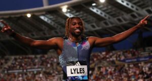Noah Lyles raises his hands in the air to a packed stadium crowd