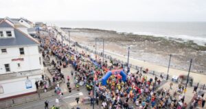 Aeriel view of thousands of runners at the start line of the race by the sea