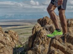 Man stands on rocky ledge high above desert wearing green shoes