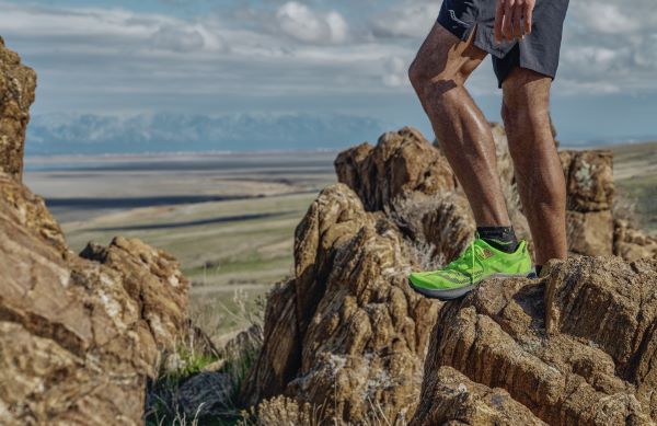 Man stands on rocky ledge high above desert wearing green shoes