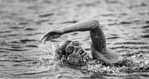 a black and white photo of a triathlete swimming front crawl in open water.