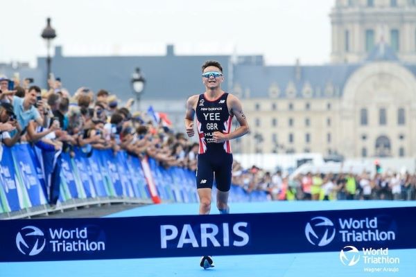 Alex Yee runs towards the finish tape of the Olympic Games Paris Test Event, which has the words World Triathlon Paris on it.