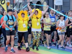 Two ladies dressed as sunflowers, and a male runner in a blue t-shirt and black shorts lead a pack of runners onto a road painted with a rainbow.