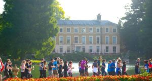 Runners run in front of a stately home surrounded by manicured gardens