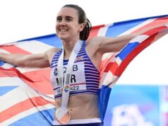Laura Muir smiles as she wears a medal around her neck, and holds a union flag outstretched across her shoulders.