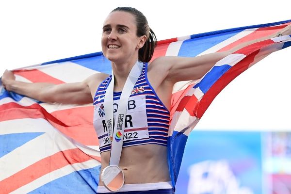 Laura Muir smiles as she wears a medal around her neck, and holds a union flag outstretched across her shoulders.