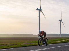 Lone triathlete cycles past two wind turbines in a flat landscape