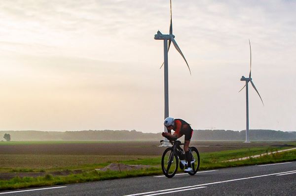 Lone triathlete cycles past two wind turbines in a flat landscape