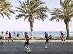 Triathletes run along a seafront promenade lined with palm trees