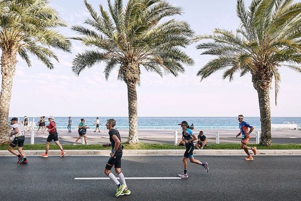 Triathletes run along a seafront promenade lined with palm trees