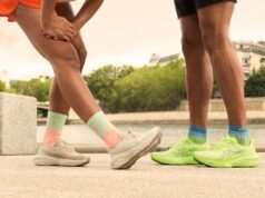 legs of a man and woman wearing shorts and running shoes. Woman is stretching out her hamstring.