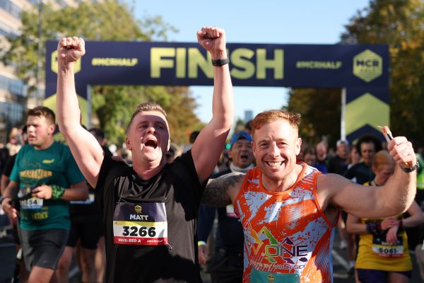 Two men cross the finish line, absolutely thrilled to have finished. One man roars with joy, arms in the air.