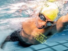 Male athlete swims through water. He wears yellow swim cap and goggles. We can see the data that is displayed on his goggles.
