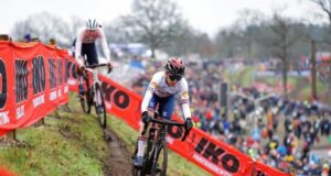 A female cyclist contours a steep muddy bank, followed by another competitor.