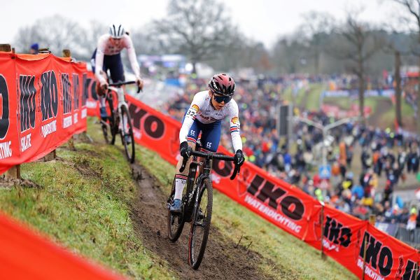 A female cyclist contours a steep muddy bank, followed by another competitor.