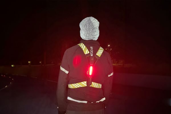 A male runner seen from behind wears a reflective beanie and an X-shaped reflective vest with a red light on the back