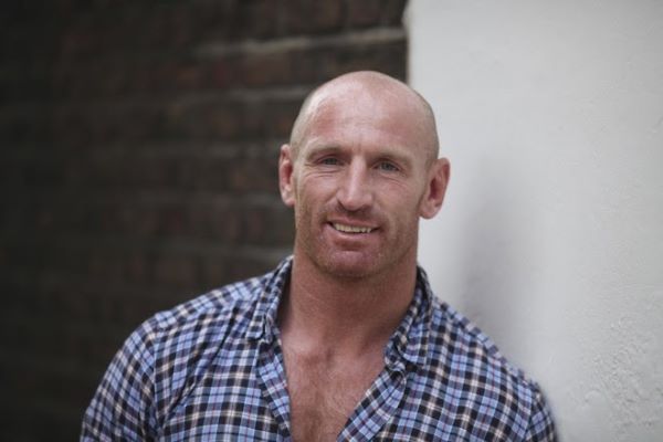 Head and shoulders of man with close shaved head wearing checked shirt open at the chest.
