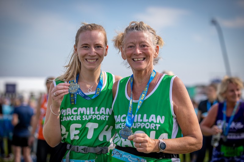 Two Great North Run Finishers, both ladies holdding their medals, smiling for the cameera and wearing their green Macmillan running vests