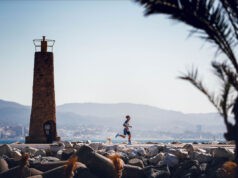 Man runs near a brick lighthouse on the coast