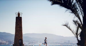Man runs near a brick lighthouse on the coast
