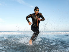 A triathlete in a wetsuit runs out of the sea