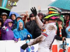 Cyclist in very muddy jersey throws an item into the crowd