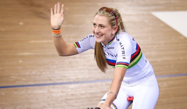 Laura Kenny in white cycling kit on her track bike waves to the crowd with a smile on her face