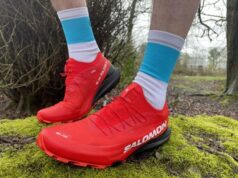 Very clean red trail shoes, on the feet on a runner, standing on a mossy rock in woodland, about to head off for a trail run.